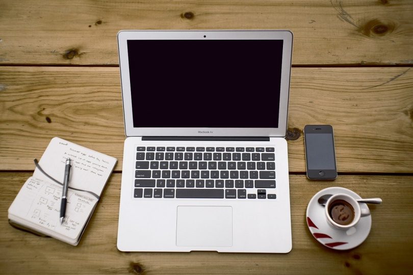 Mesa de trabalho com notebook, café, caderno e celular