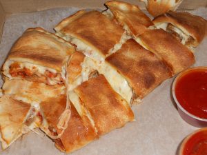 Imagem de vários pedaços de calzone ao lado de molhos de tomate