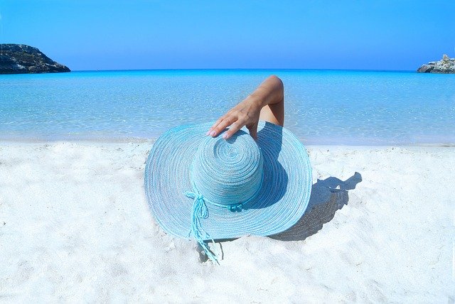 Pessoa deitada na areia com um chapéu de sol azul