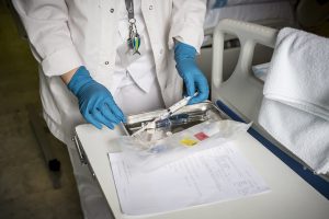 Médica de uniforme branco com seringa na mão e outros utensíios sobre formulário