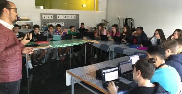 Imagem de alunos com pequenos computadores à frente sobre mesas