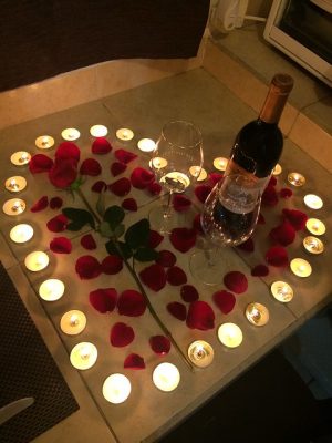 Imagem de garrafa de vinho, pétalas de rosa e velas acesas