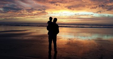 Pai e filho observam as cores do entardecer numa praia