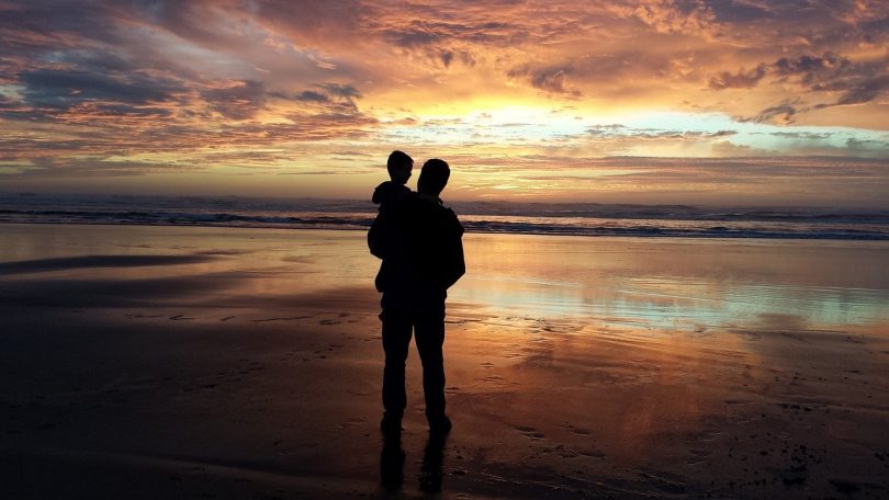 Pai e filho observam as cores do entardecer numa praia